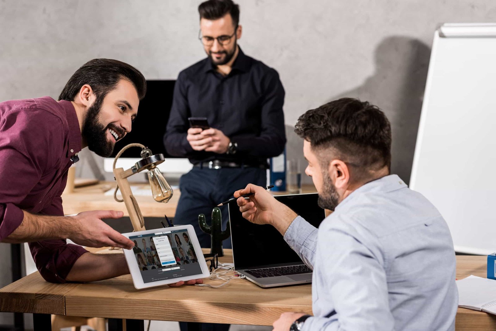 smiling businessman showing colleagues linkedin page on tablet